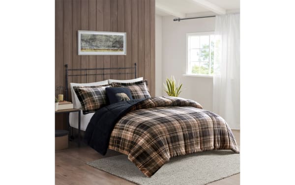 Modern bedroom with a black metal bed frame and plaid bedding in shades of brown, beige, and black, featuring a cozy black throw blanket and matching pillows.