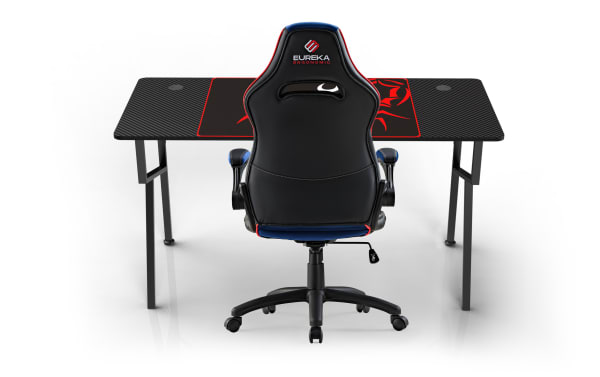 Black Eureka Ergonomic gaming chair with blue and red accents, high backrest, adjustable armrests, positioned in front of a black carbon fiber gaming desk with red design.