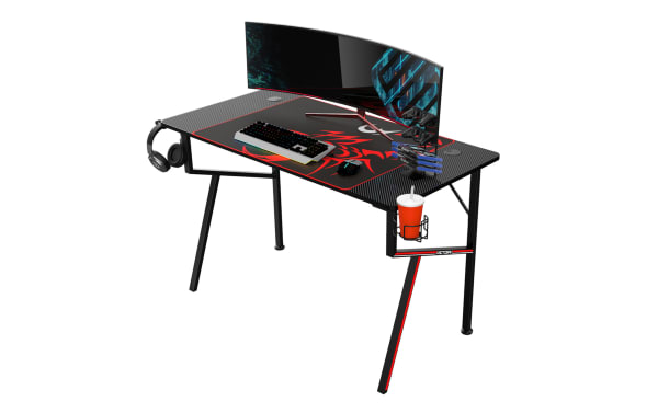 Black and red Victory gaming desk with carbon fiber textured surface, curved widescreen monitor, RGB keyboard, mouse, headset hook, and cup holder.