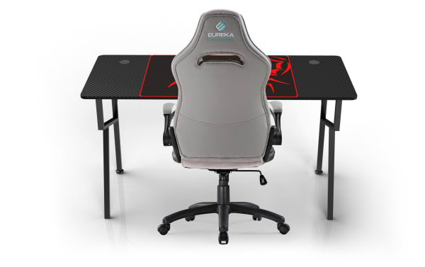 Ergonomic gray Eureka gaming chair with light blue logo text "EUREKA ERGONOMIC" on backrest, paired with black carbon fiber style gaming desk with red dragon design and cable management holes.