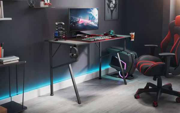 Kai Black Gaming Desk in transitional style with black powder-coated metal legs and carbon-fiber particle board surface, featuring full-size mouse pad, headset hook, cup holder, gamepad rack, and built-in cable management for an organized gaming or streaming setup.