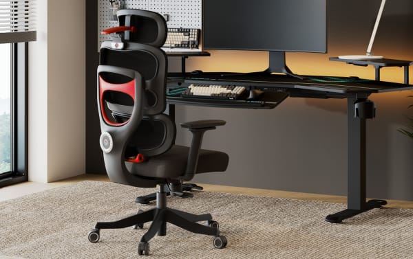 Modern ergonomic black and red mesh office chair with adjustable armrests and wheels, positioned at a sleek black standing desk with dual monitors and keyboard.