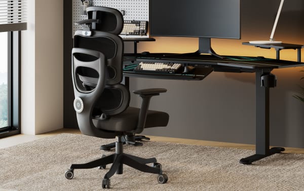Ergonomic black mesh office chair with adjustable headrest and lumbar support, paired with a modern black standing desk setup featuring a large curved monitor and keyboard tray.