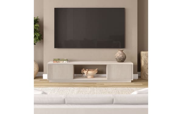 Modern beige TV stand with ribbed cabinet doors, decorative pottery, and books under a wall-mounted flat-screen TV in a cozy living room.