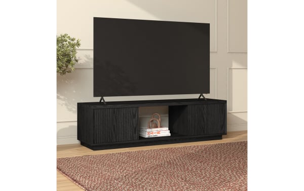 Modern black wooden TV stand with ribbed cabinet doors, open central shelf holding books and decor, supporting a large flat-screen TV in a bright living room.