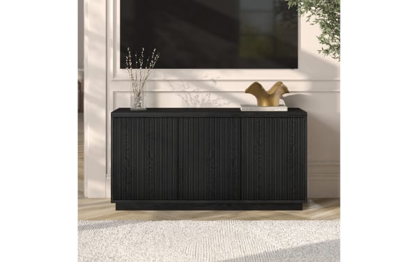 Black wooden sideboard with vertical grooves, minimalist design, flat top holding a glass vase with branches and a gold decorative sculpture on a book titled "LINEN".