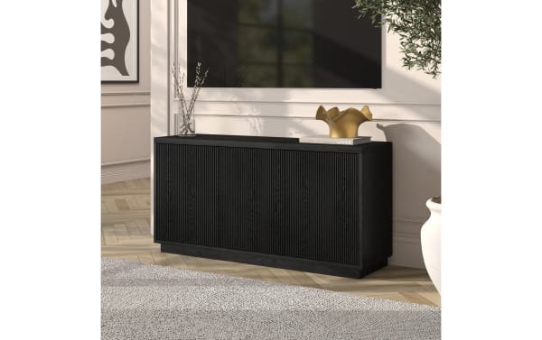 Black wooden sideboard with vertical grooves, minimalist design, and decorative gold vase and book on top, set in a modern living room.