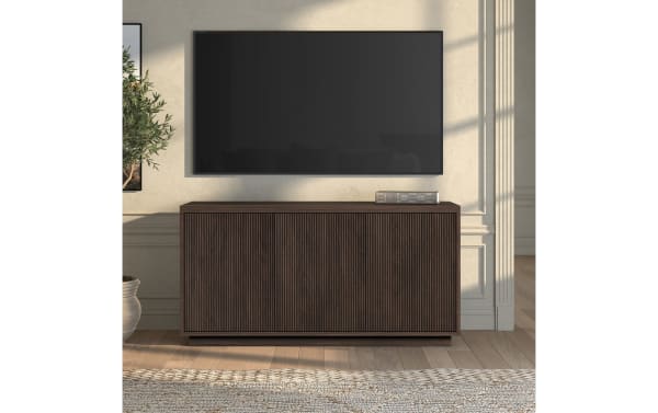 Dark brown wooden TV console with vertical grooves and a flat top, placed under a wall-mounted flat-screen TV in a modern living room.