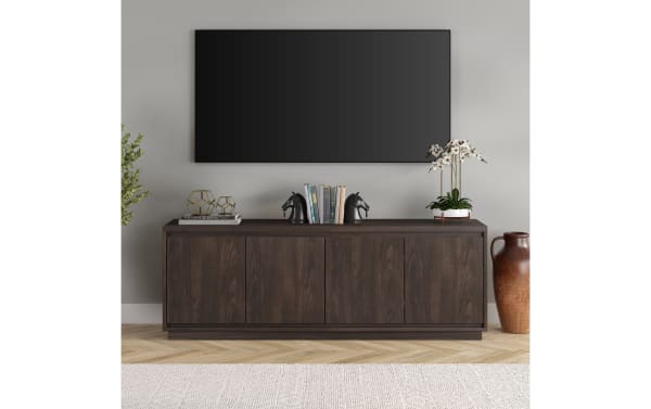 Dark wood TV console with four cabinet doors, decorated with black horse bookends, books, geometric sculptures, and a white orchid plant, beneath a wall-mounted flat-screen TV.