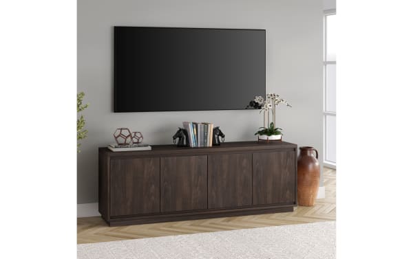 Dark wood TV console with four cabinet doors, decorative horse bookends holding books, geometric sculptures, and a potted orchid under a wall-mounted flat-screen TV.