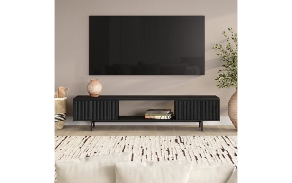 Modern living room setup with a wall-mounted flat-screen TV above a black wood TV console featuring ribbed cabinet doors, open shelving with books, and decorative vases on either side.