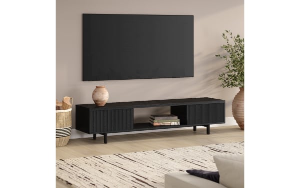 Modern black wooden TV stand with slatted cabinet doors and open shelf, styled with decorative vases and books, in a minimalist living room.