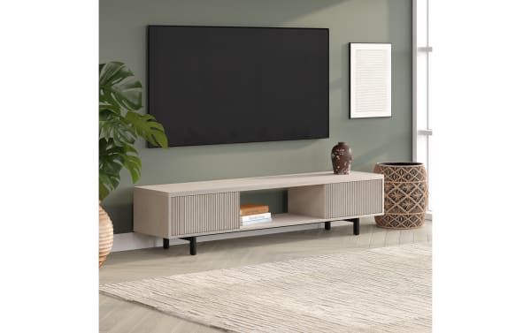 Modern light wood TV stand with black metal legs, featuring ribbed sliding doors, open shelf with books, and decorative vase, under wall-mounted flat screen TV.