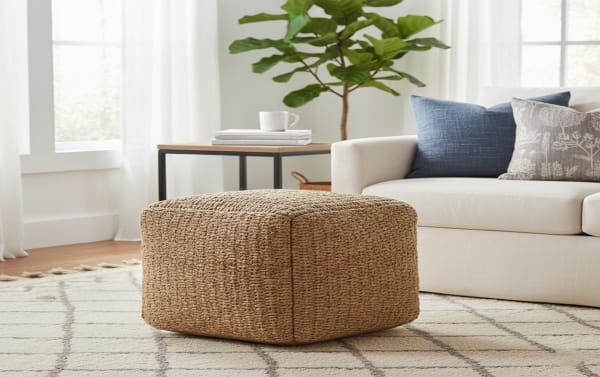 Esme Brown Pouf in farmhouse style, handcrafted brown jute cube-shaped ottoman for seating or footrest, placed on patterned rug in living room.