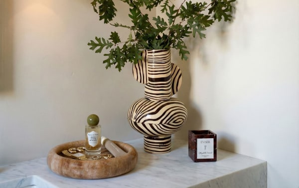 Contemporary 10'' Elix Light Brown Round Marble Tray in polished onyx, styled with gold jewelry and perfume on a marble surface, showcasing sleek natural elegance.