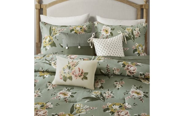 Green floral bedding set with large yellow and pink flowers, striped and patterned accent pillows, and a wooden headboard, showcasing a cozy, vintage-inspired bedroom style.