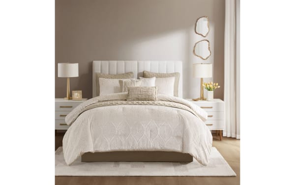 King-size bed with beige quilted comforter and pillows, upholstered headboard, white nightstands with gold lamps, beige walls, and decorative mirrors.