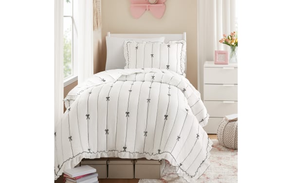 White comforter set with black vertical lines and bow patterns, featuring ruffled edges, on a twin bed in a cozy bedroom setting.
