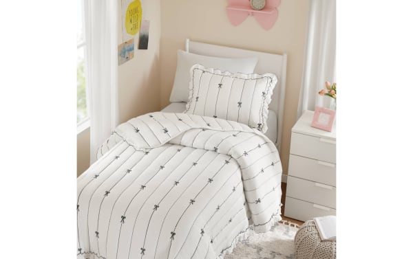 White twin bed with a soft quilted comforter and pillow featuring black vertical lines and small bow patterns, in a cozy bedroom setting.