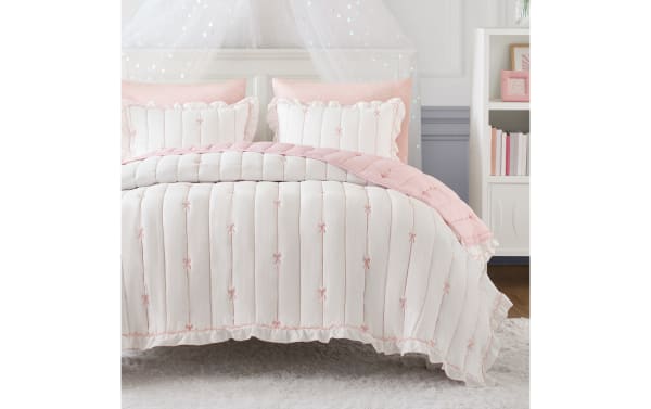 Maison Full/Queen Pink 3 Piece Quilt Set with white microfiber, pink bow embroidery, ruffled edges, and down-alternative fill for cozy, stylish bedding.