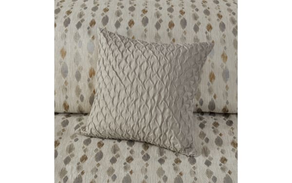 Beige decorative throw pillow with a textured, tufted diamond pattern on a fabric sofa with a multicolor abstract dotted design in neutral tones.