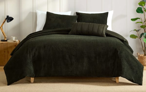 Dark green ribbed corduroy bedding set with matching pillows on a bed, styled in a modern bedroom with wooden nightstand and plant.