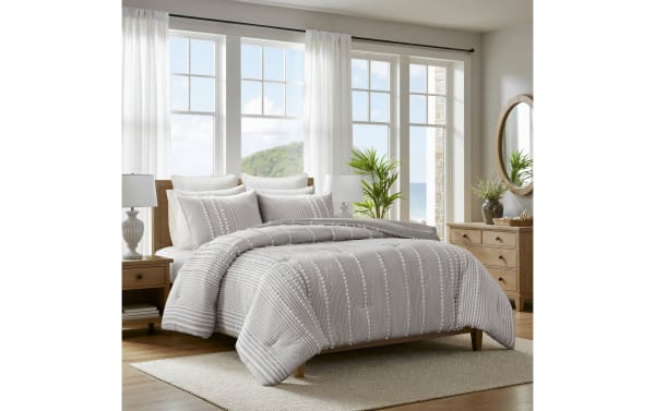 Gray and white striped textured comforter set on wooden bed frame in bright bedroom with large windows, wooden furniture, and neutral decor.