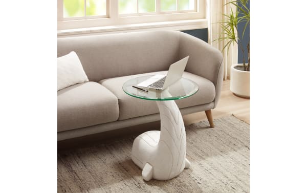 Modern living room with a beige fabric sofa, a white whale-shaped side table with a glass top, a laptop, and a gray textured rug.