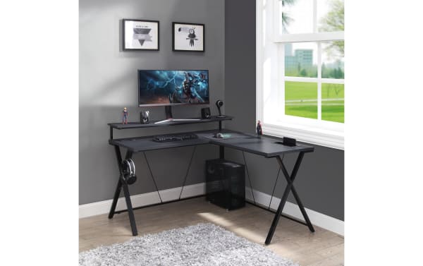 Chuck Gray L-Shaped Gaming Desk in black painted steel and MDF with built-in power outlet, dual USB ports, wireless charging pad, LED lights, upper monitor shelf, accessory hook, cup holder, and lower tower shelf, designed for home office and gaming setups in a sleek transitional style.