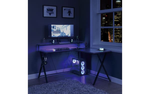 Chuck Gray L-Shaped Gaming Desk in sleek transitional style with steel and MDF construction, built-in power outlet, USB ports, wireless charging pad, LED lights, upper monitor shelf, accessory hook, cup holder, and lower tower shelf.