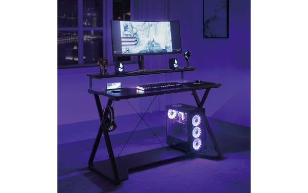Chuck Gray Gaming Desk in black steel and MDF with transitional style, featuring dual monitor shelf, RGB LED lights, USB ports, wireless charger, cup holder, accessory hook, and lower tower shelf for organized gaming setup.