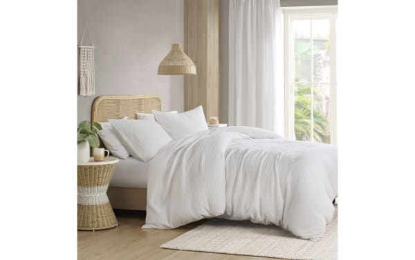 Bed with white cotton duvet cover and pillows, featuring a rattan headboard and matching side table, set in a bright, modern bedroom.