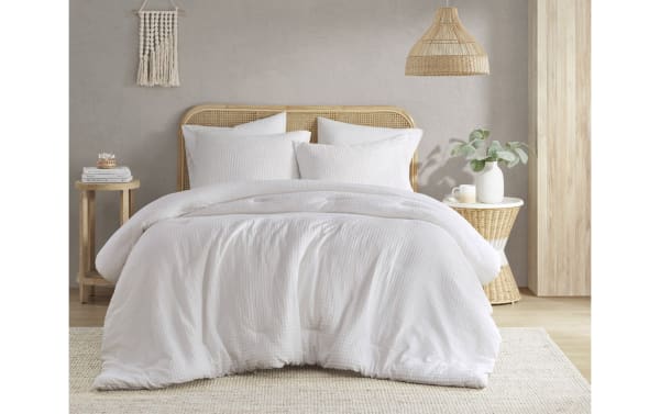 White cotton comforter set on a rattan bed frame with matching pillows in a neutral, minimalist bedroom setting.