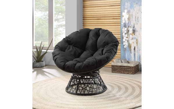 Black cushioned papasan chair with a woven rattan base, placed on a round beige rug in a modern living room setting.