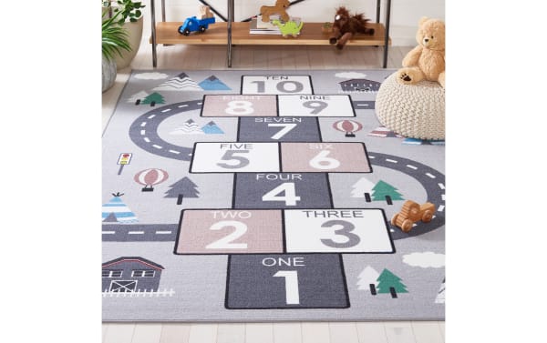 Children's hopscotch rug in gray with numbered squares one to ten, featuring road and tree illustrations, soft woven fabric for playrooms.