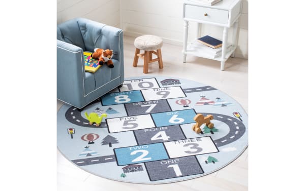 Happy Hopper 3' round light blue rug with playful hopscotch and road pattern, soft polyamide fabric, slip-resistant backing, and washable design for kids.