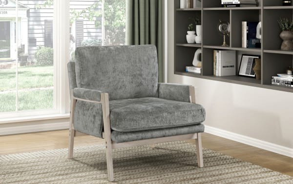 Gray upholstered armchair with light wood frame, featuring plush cushions and mid-century modern design, placed on a textured rug near a window.