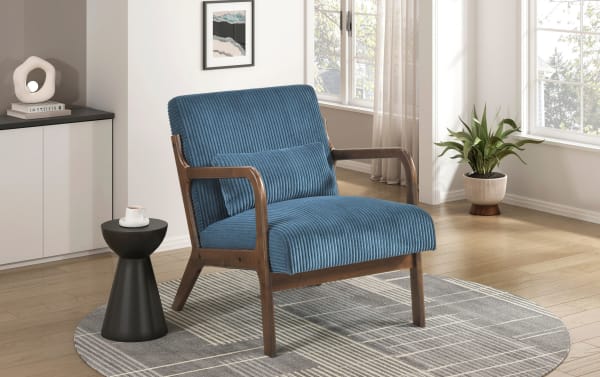 Blue corduroy upholstered mid-century modern armchair with wooden frame, matching lumbar pillow, black side table with white cup, gray patterned round rug, and potted plant in bright living room.