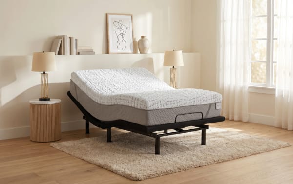 Adjustable split queen mattress with white and gray memory foam on black metal frame, placed on beige shag rug in bright modern bedroom.
