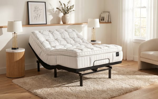 Adjustable white tufted mattress on black metal frame in a modern bedroom with wooden floors, beige rug, and soft lighting.