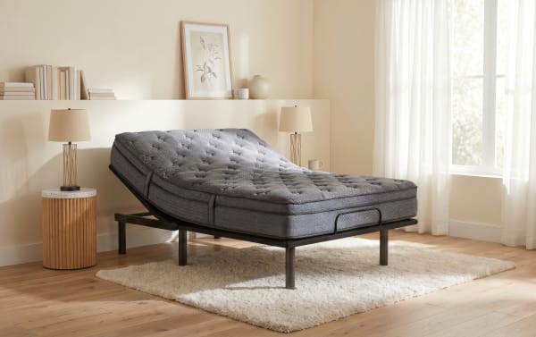 Adjustable gray mattress on a black metal frame with a quilted top, set on a beige shag rug in a bright, modern bedroom.