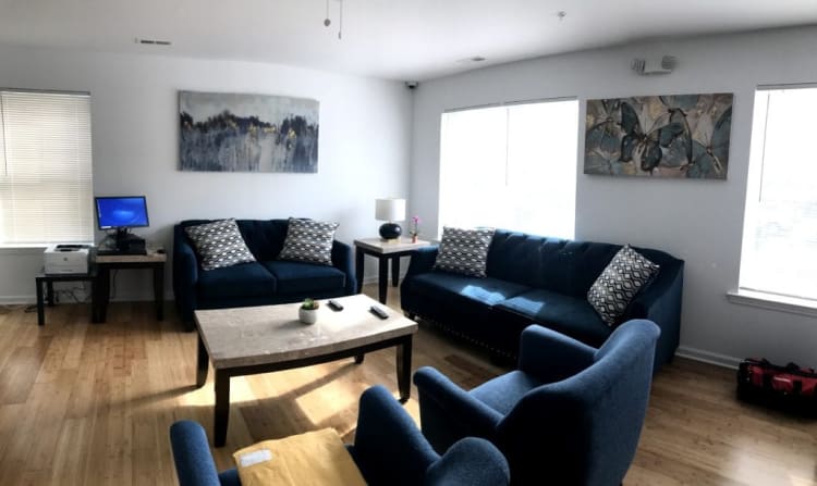 Living room with blue velvet sofas and armchairs, wooden floor, marble coffee table, side tables with lamps, and wall art featuring abstract and butterfly designs.