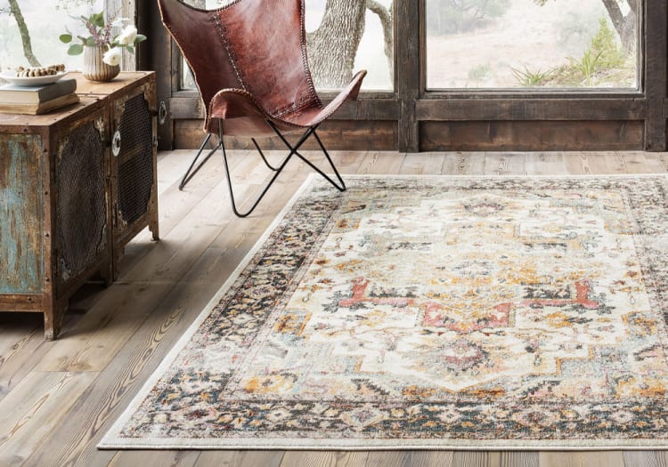 Rustic living room corner with a distressed wooden cabinet, brown leather butterfly chair, and a vintage-style patterned area rug on light wood flooring.