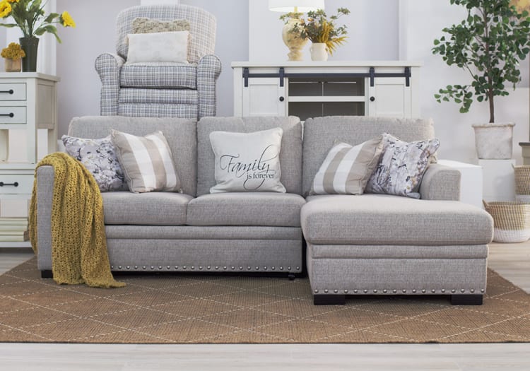 Gray fabric sectional sofa with chaise lounge, decorative pillows including one with "Family is forever" text, mustard knit throw, and a patterned area rug in a modern living room setting.