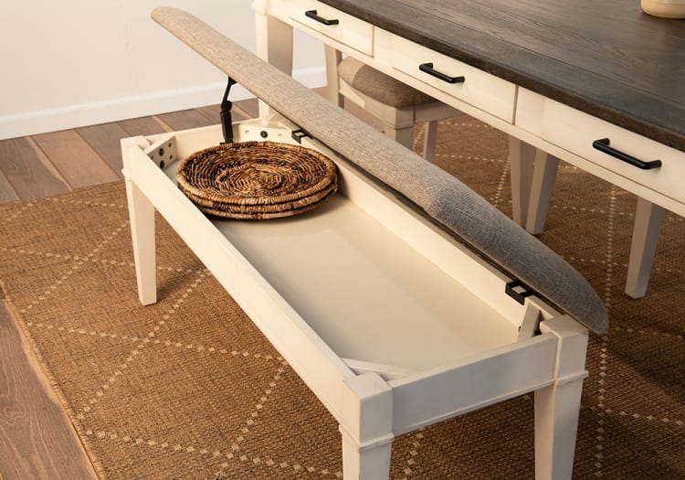 Upholstered storage bench with beige fabric cushion, white wooden frame, and woven basket inside, placed on a textured brown rug.