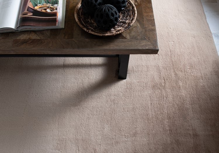 Dark wood coffee table with black metal legs on a beige textured carpet, featuring a woven basket with decorative black spheres and an open cookbook.