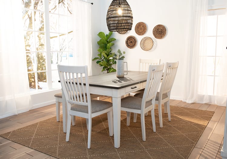 Dining room with white wooden table featuring a dark tabletop, four matching chairs with gray cushions, woven pendant light, and decorative wall baskets.