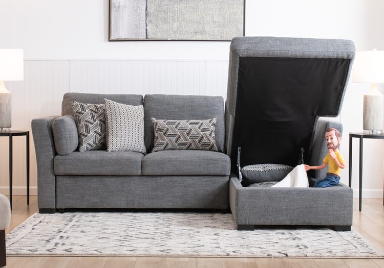 Gray fabric sectional sofa with storage ottoman open, patterned throw pillows, modern side tables with lamps, and a light geometric rug in a living room.