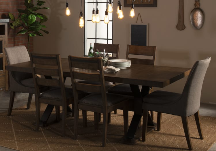 Dining room with a dark wood rectangular table and six mixed-style chairs, featuring fabric upholstery and wooden frames, under hanging Edison bulb lights.