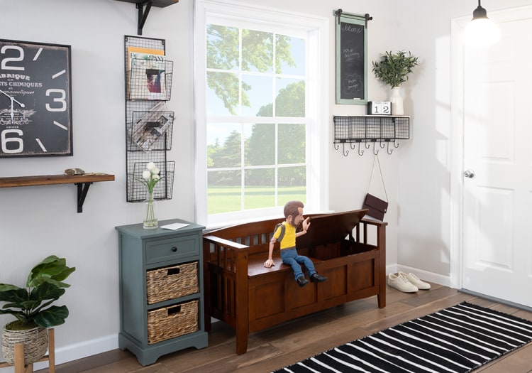 Cozy entryway with a wooden storage bench featuring lift-up seat, blue cabinet with wicker drawers, black and white striped rug, and wall decor including a large clock and calendar.